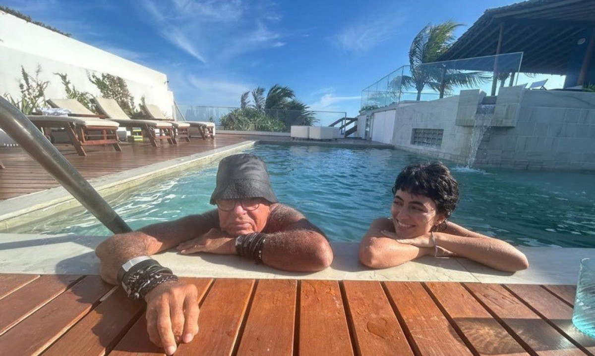 O m&uacute;sico C&eacute;zar Mendes e a cantora Loulu Gilberto est&atilde;o lado a lado, dentro da piscina, e sorriem para a c&acirc;mera. Ao fundo v&ecirc;-se o c&eacute;u azul