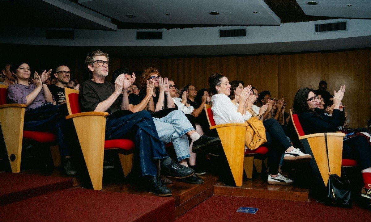 Os m&uacute;sicos Fernanda Takai e John Ulhoa e o ator Paulo Andr&eacute; est&atilde;o sentados na plateia e batem palmas durante o lan&ccedil;amento da Utup&ecirc; Oficina Sonora, na Biblioteca P&uacute;blica Estadual de Minas Gerais 