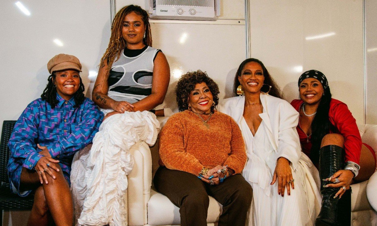  As cantoras Nubia, Melly, Alcione, Luedji Luna e Duquesa est&atilde;o lado a lado, sentadas em sof&aacute;, sorrindo para a c&acirc;mera