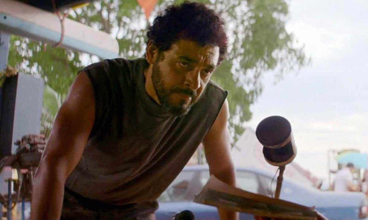 Ator Rui Ricardo Diaz tem as duas m&atilde;os sobre mesa em cena rodada na floresta no filme Anaconda 
