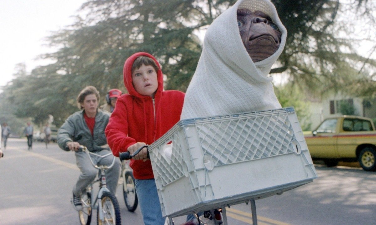  Ator mirim Henry Thomas pedala bicicleta, vestido com moletom vermelho, e carrega o alien ET numa cesta em cena do filme ET - O extraterrestre