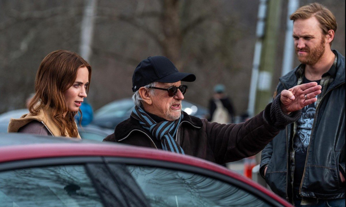 Steven Spielberg (ao centro da foto) aponta com o bra&ccedil;o para a frente, ao dirigir os atores Emily Blunt e Wyatt Russel no set de Dia D 