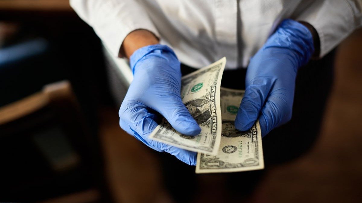 M&atilde;os enluvadas segurando notas de d&oacute;lar ilustram o manuseio de dinheiro em opera&ccedil;&otilde;es de lavagem de recursos il&iacute;citos. -  (crédito: magnific)