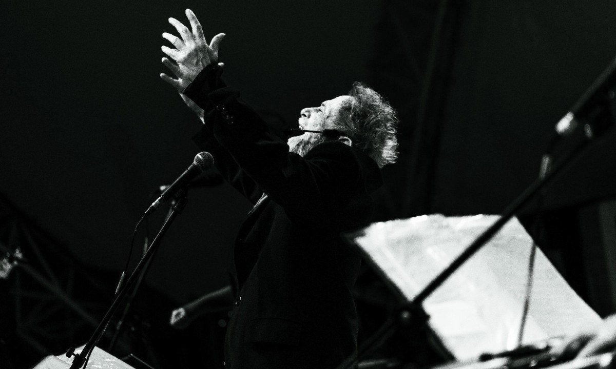 Tom Z&eacute; est&aacute; de perfil com os bra&ccedil;os levantados, cantando, durante show realizado no Distrito Federal