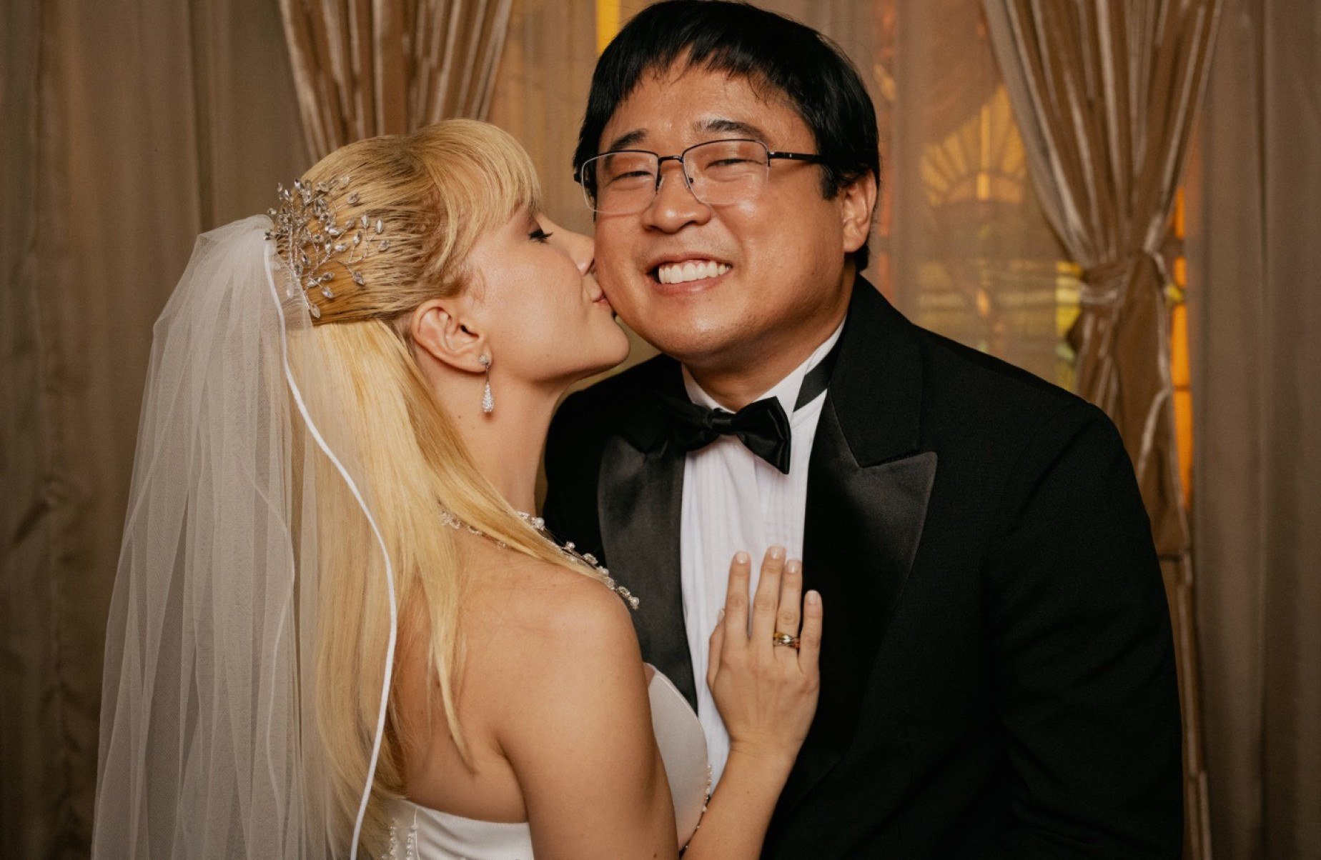Atriz Lorena Comparato, vestida de noiva, beija o ator Henrique Kimura em foto de casamento durante cena do filme Elize: Sombras de uma mulher  