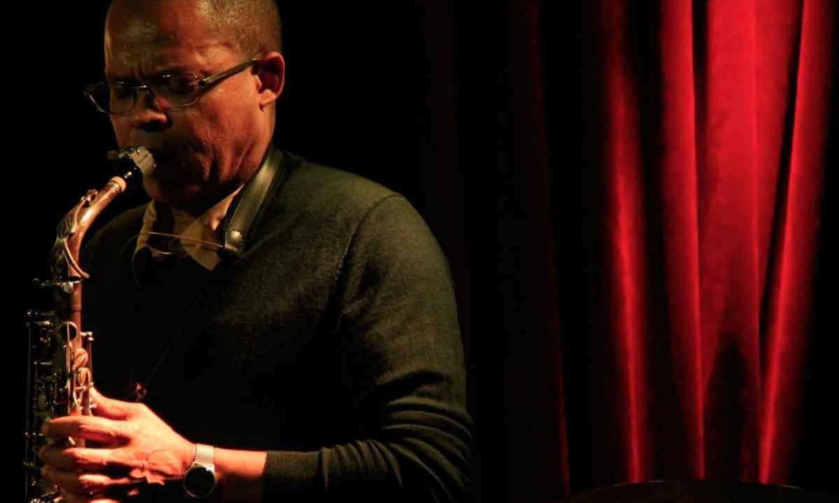 O saxofonista camaron&ecirc;s Nat Su toca no palco, tendo atr&aacute;s de si cortina vermelha