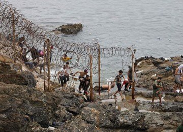 Migrantes tentam cruzar a fronteira entre Marrocos e Ceuta por uma &aacute;rea costeira rochosa com barreiras de arame farpado -  (crédito: AFP)