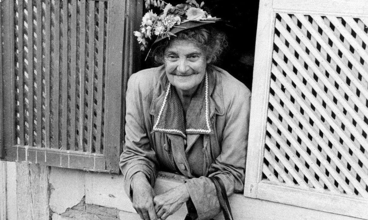 Dona Olympia em Ouro Preto, fotografada por Eug&ecirc;nio Silva para a revista O Cruzeiro, em 1957. Ela usa chap&eacute;u de flores e est&aacute; debru&ccedil;ada em janela de casar&atilde;o de Ouro Preto