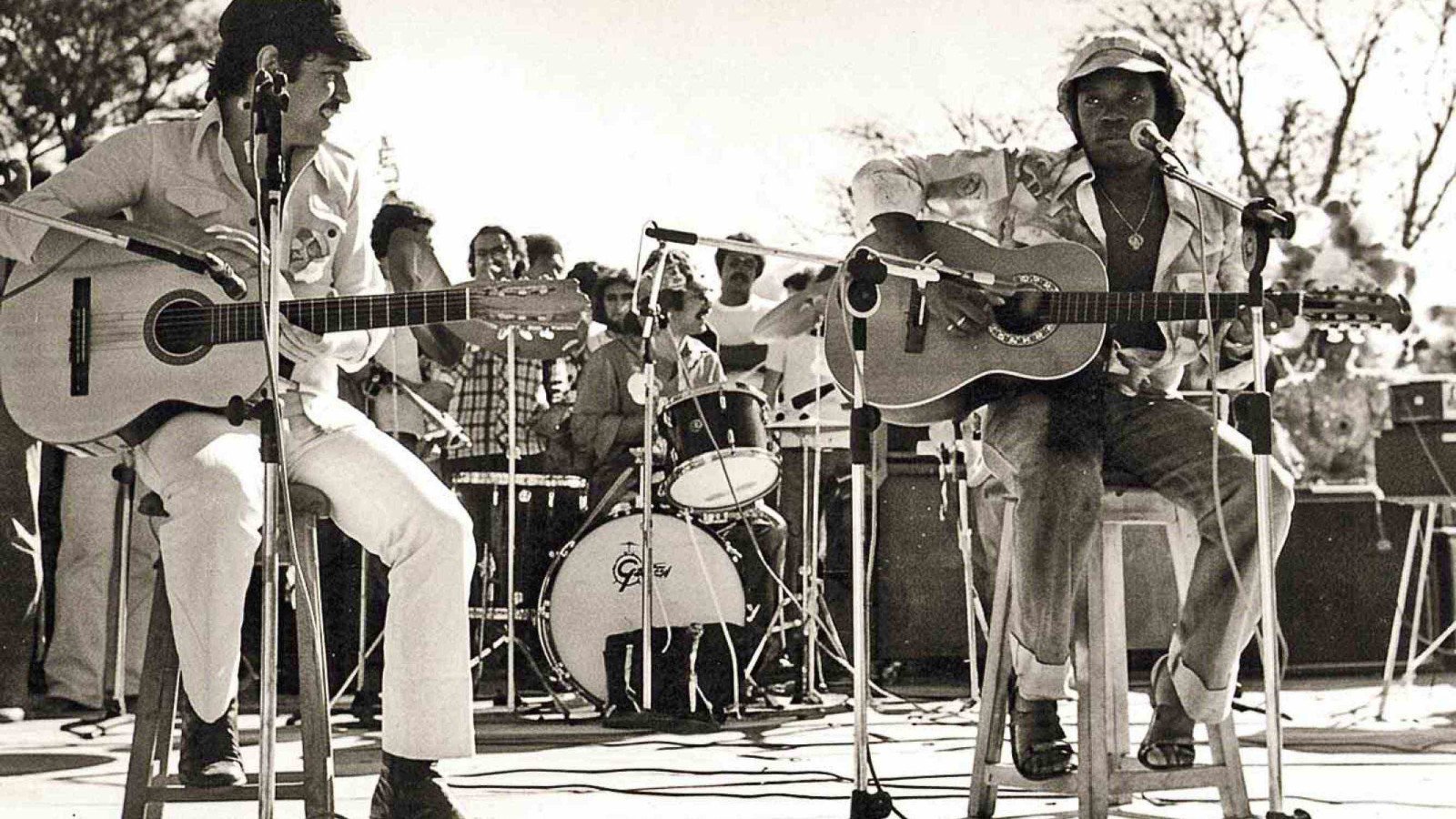 Chico Buarque e Milton Nascimento, sentados em bancos, tocam viol&atilde;o e cantam no evento que ficou conhecido como Woodstock mineiro, em Tr&ecirc;s Pontas, em 1977