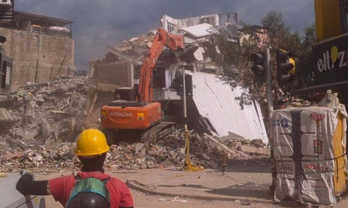Voluntário observa enquanto máquina derruba prédio vizinho a uma edificação colapsada na qual, até dois dias antes, procuravam-se sobreviventes em Pereira, na Colômbia - (crédito: Phillippe Watanabe/Folhapress)