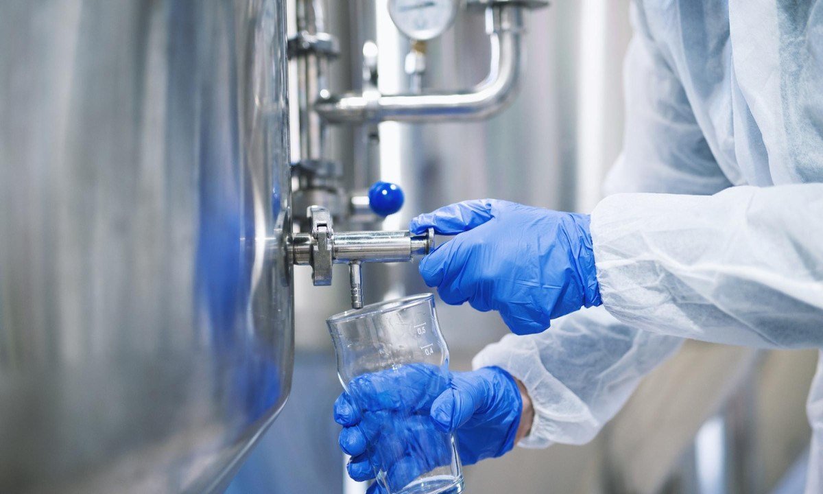 Close up view of hands in protective gloves opening tap valve and filling glass with samples from industrial machine reservoir.
- (crédito: DINO)