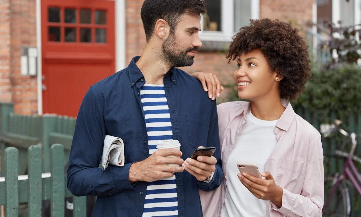 Satisfied woman and her boyfriend of different nations exchange telephone numbers, hold modern smart phones, stands outdoor with takeaway coffee, have accidental meeting on street in village
- (crédito: DINO)