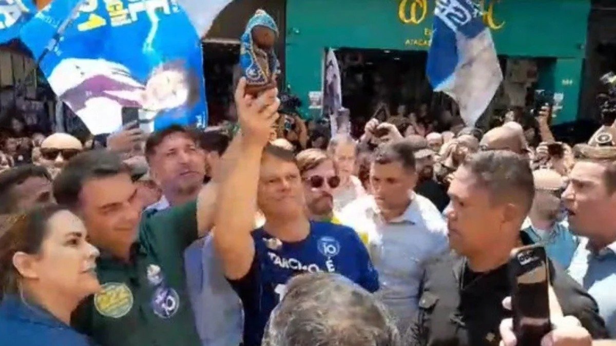 Fl&aacute;vio Bolsonaro e Tarc&iacute;sio de Freitas em ato de campanha onde imagem de Nossa Senhora Aparecida &eacute; exibida, reacendendo debate sobre uso religioso na pol&iacute;tica -  (crédito: Reprodu&ccedil;&atilde;o/G1)