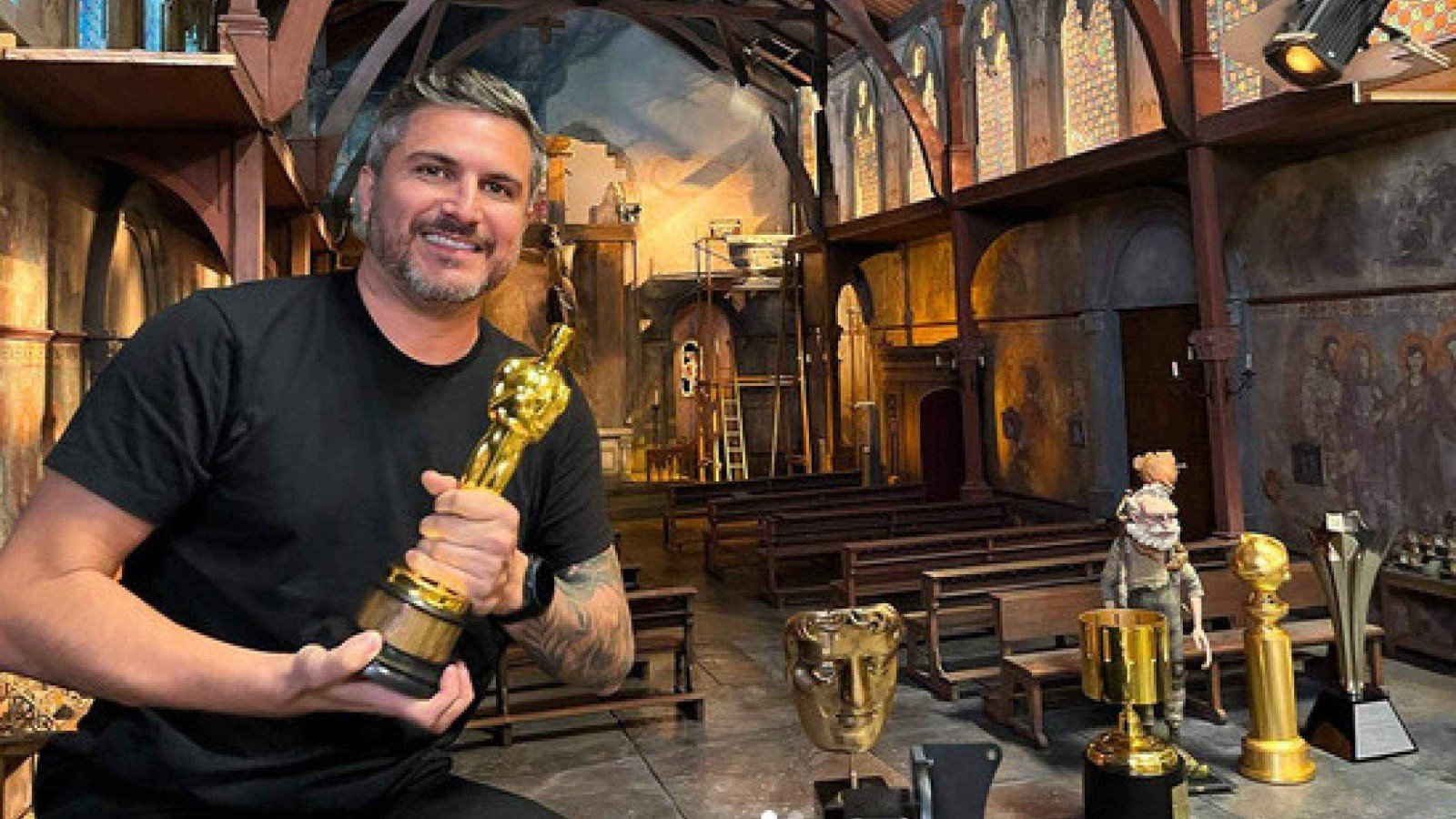 Animador Thiago Cal&ccedil;ado segura estatueta do Oscar ao lado de mesa onde se veem v&aacute;rios trof&eacute;us que ele ganhou