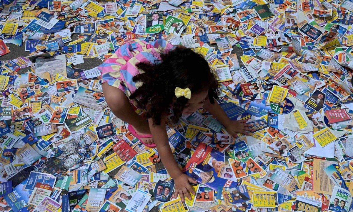 Menina brinca com santinhos de candidatos no primeiro turno das eleições, na Cidade de Deus, no Rio de Janeiro -  (crédito: TERCIO TEIXEIRA / AFP)