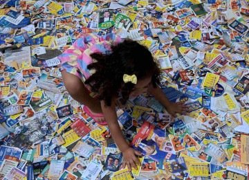 Menina brinca com santinhos de candidatos no primeiro turno das eleições, na Cidade de Deus, no Rio de Janeiro -  (crédito: TERCIO TEIXEIRA / AFP)
