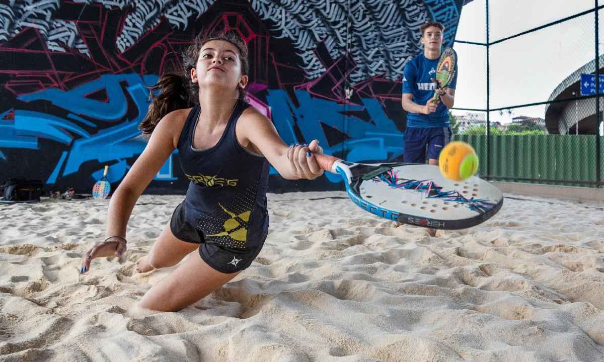 Duas crianças, uma menina a frente se jogando a areia para alcançar uma bolinha, e um menino atrás em pé, jogando beach tênis -  (crédito: Divulgação/ Viaduto das Artes)